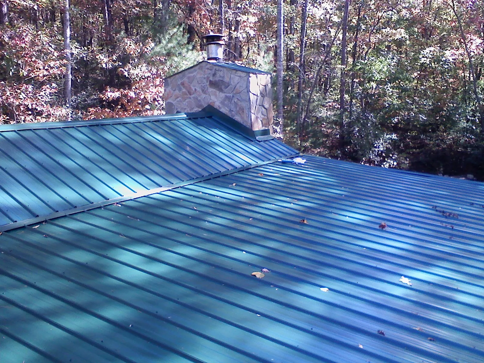 New green metal roof and stone chimney surrounded by autumn woods in Lakewood